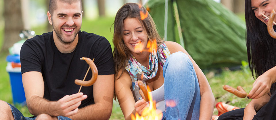 Gruppo di amici griglia salsicce sul falò di un camping altoatesino