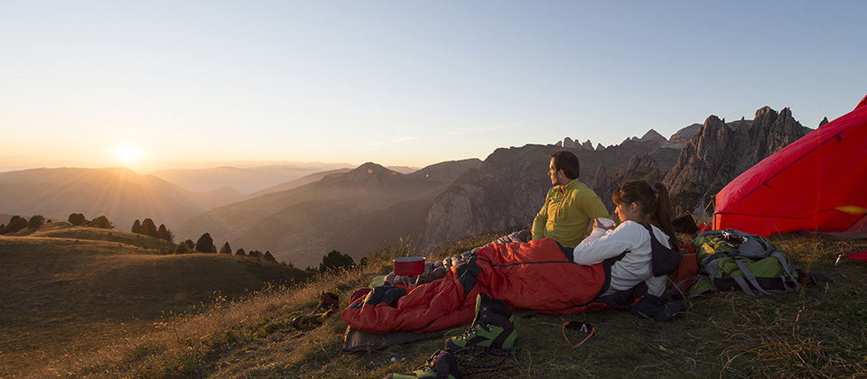 Coppia nei loro sacchi a pelo si gode il sorgere del sole nelle Dolomiti