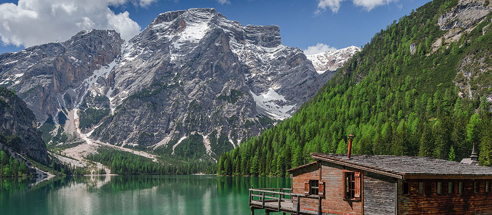 Piccola casetta di legno sul lago di Braies con montagne spolverate di neve sullo sfondo
