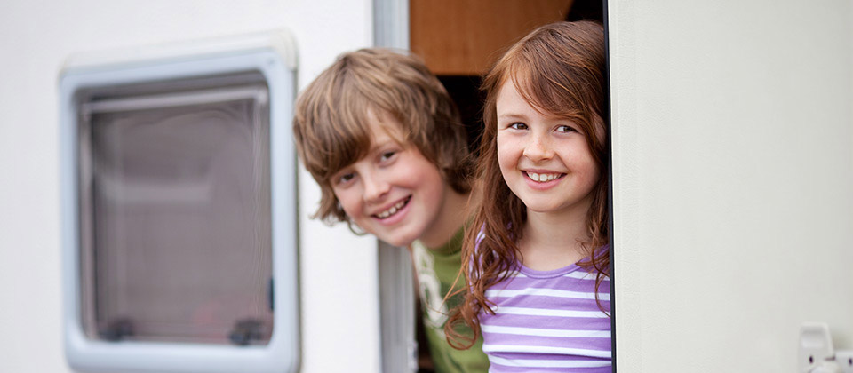 Two smiling and curious kids leaning out from a camping van