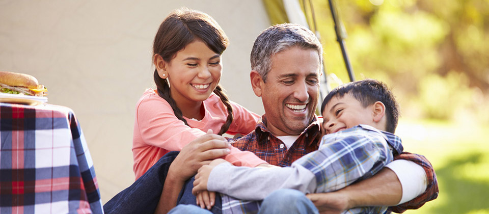 Bimbi che abbracciano il papà in un campeggio in Alto Adige davanti a una tavola imbandita