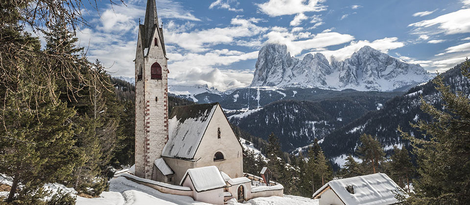 La chiesa di San Giacomo innevata con il Sassolungo come sfondo