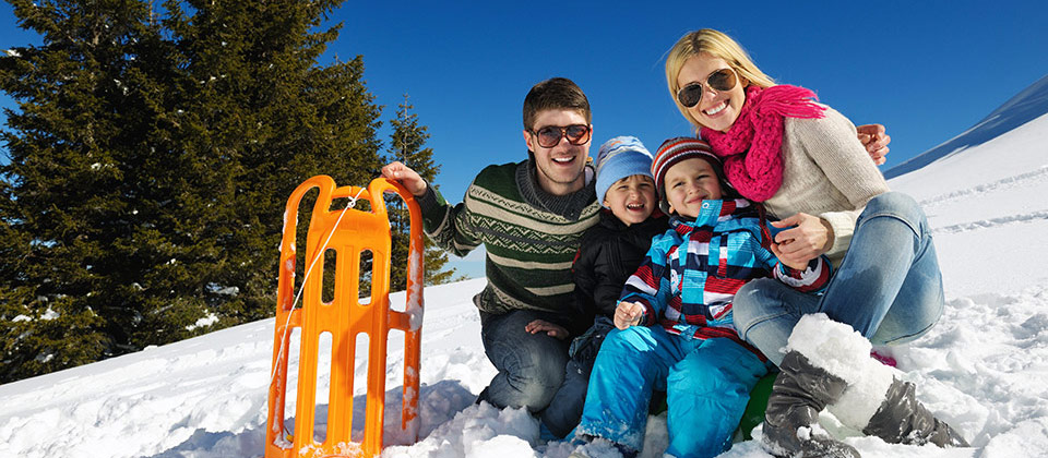 Famiglia felice che sta seduta sulla neve dopo una giornata in slitta
